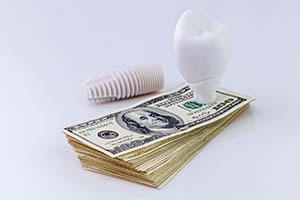 Model implant and money representing the cost of dental implants in Worcester