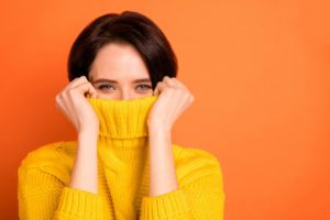 a woman wearing a yellow sweater and using it to hide her gummy smile