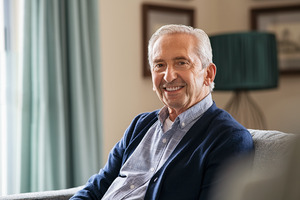 Senior man leaning forward on couch and smiling