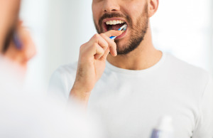Bearded man in white shirt brushing his teeth